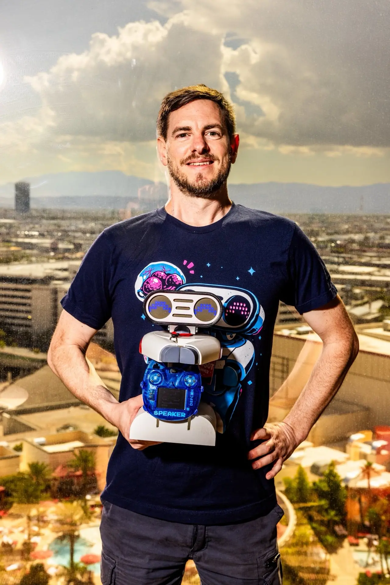 dwangoAC holding TASBot in a superhero pose in front of a window overlooking Las Vegas.