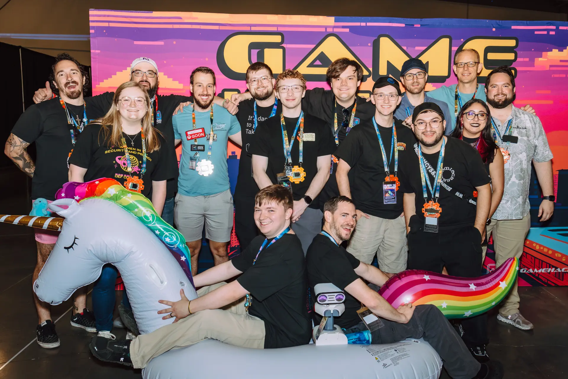 Official DEF CON photographer Game Hacking Village volunteer photo from SY Photography as posted at https://www.flickr.com/photos/switch4success/55456655096/in/album-72177720335074617/ showing the staff and volunteers in front of the Game Hacking Village banner; an inflatable unicorn with TASBot, a Game Hacking Village staff member, and dwangoAC sitting on top.